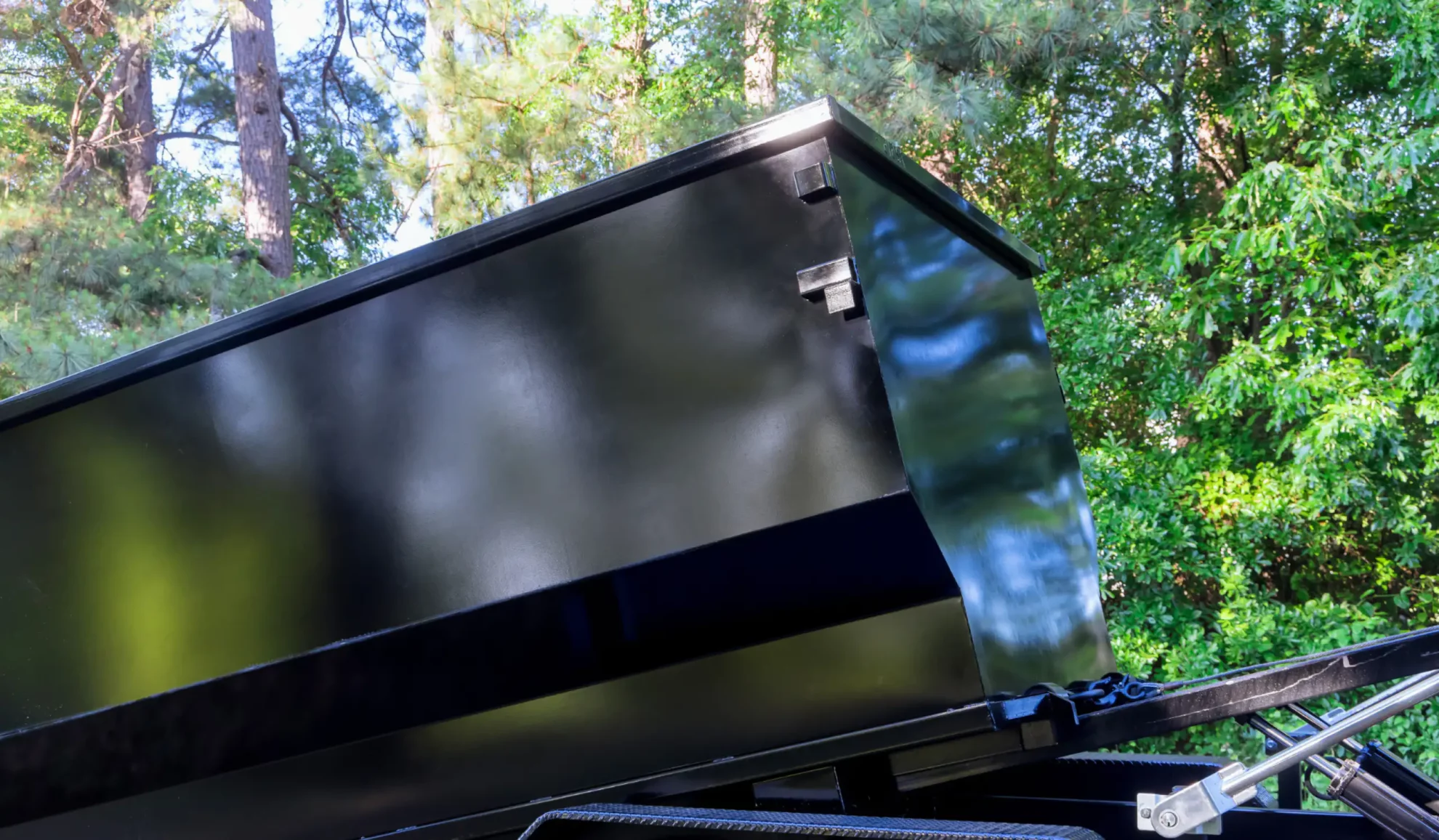 dark grey dumpster with some bushes and trees behind